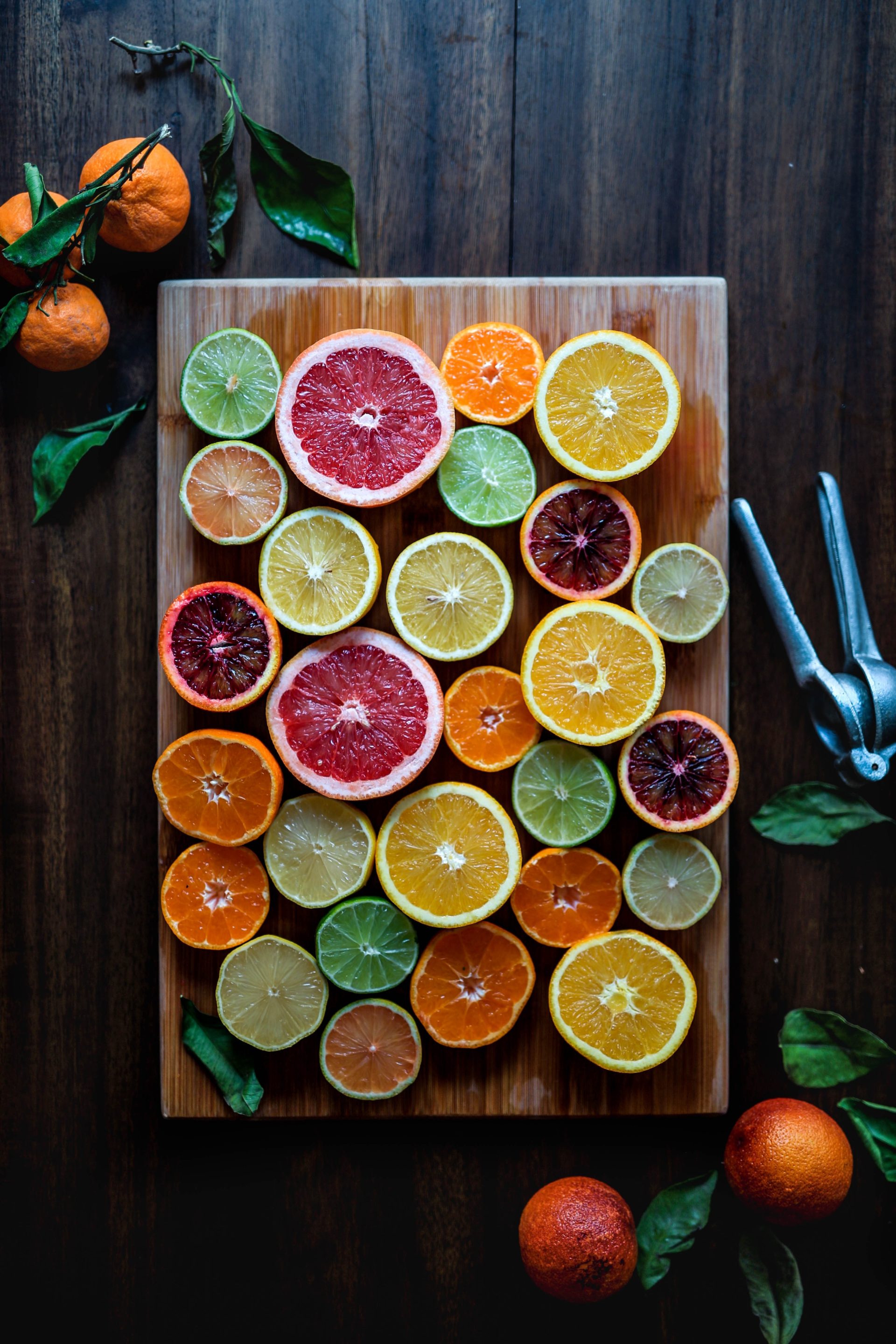 Immune boosting citrus fruits are halved and arranged on a wooden cutting board with a dark wooden table in the background.