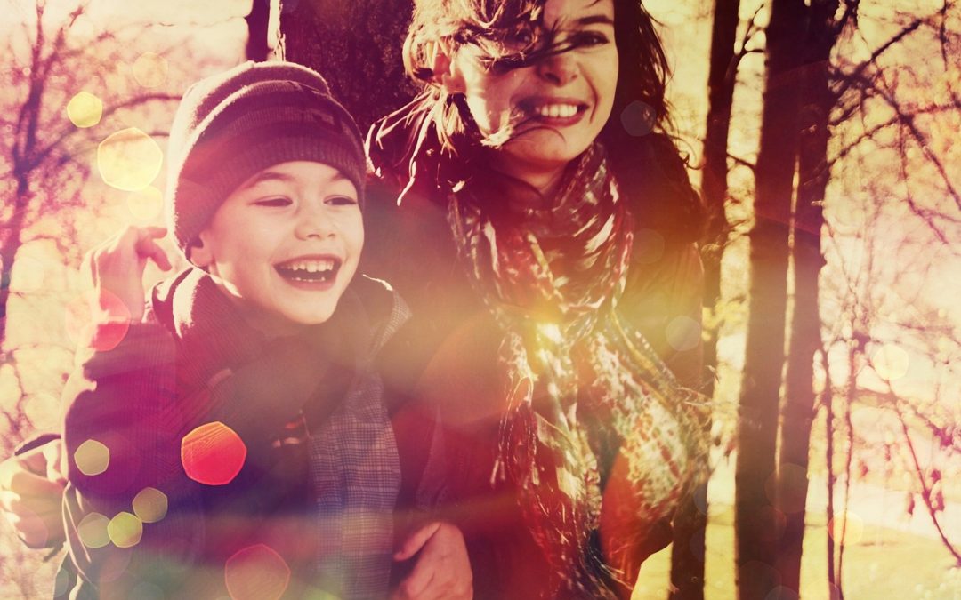 A woman and young boy are laughing towards the camera with trees in the background.
