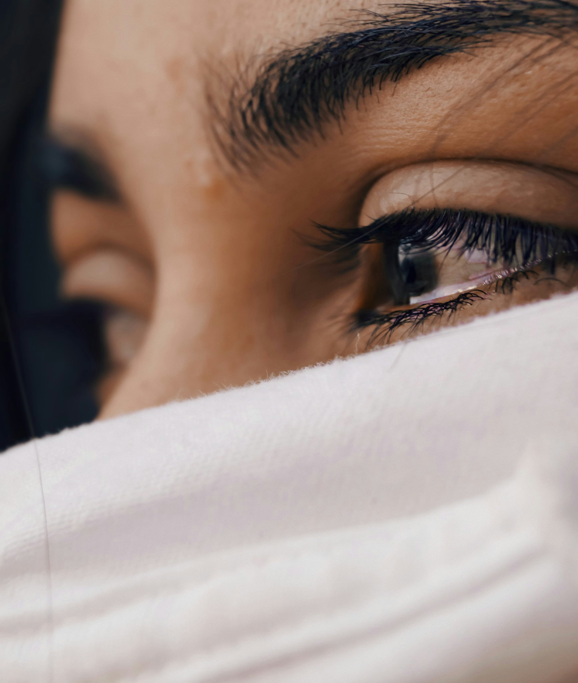 A woman's face is covered except for her tear-filled eyes, which are looking away from the camera