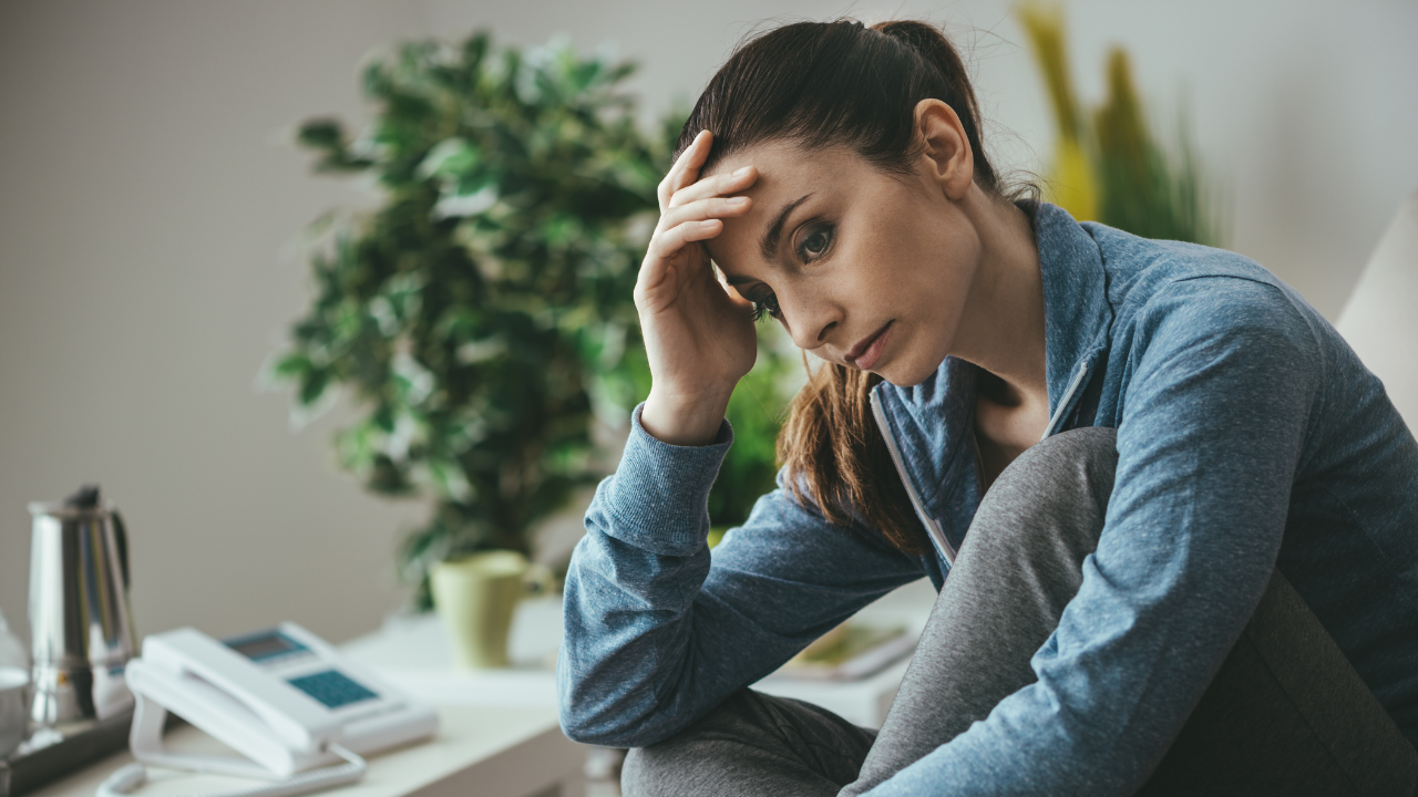 A woman holds her head in her right hand with a strained expression.