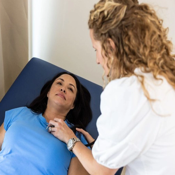 A healthcare professional uses a stethoscope to listen to the chest of a woman lying on an examination table during a medical check-up.